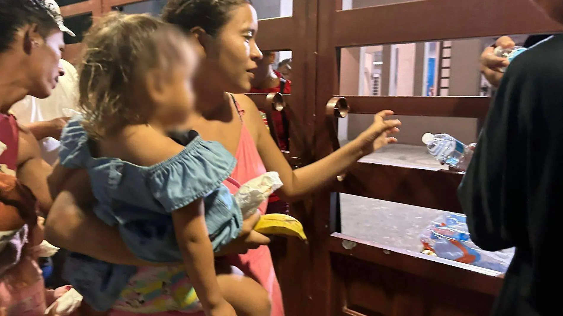 mujer migrante cargando a su hija recibiendo alimentos